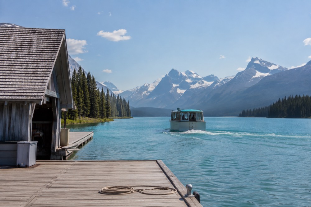 A small tour boat crossing a long glacial lake toward mountains at the far end