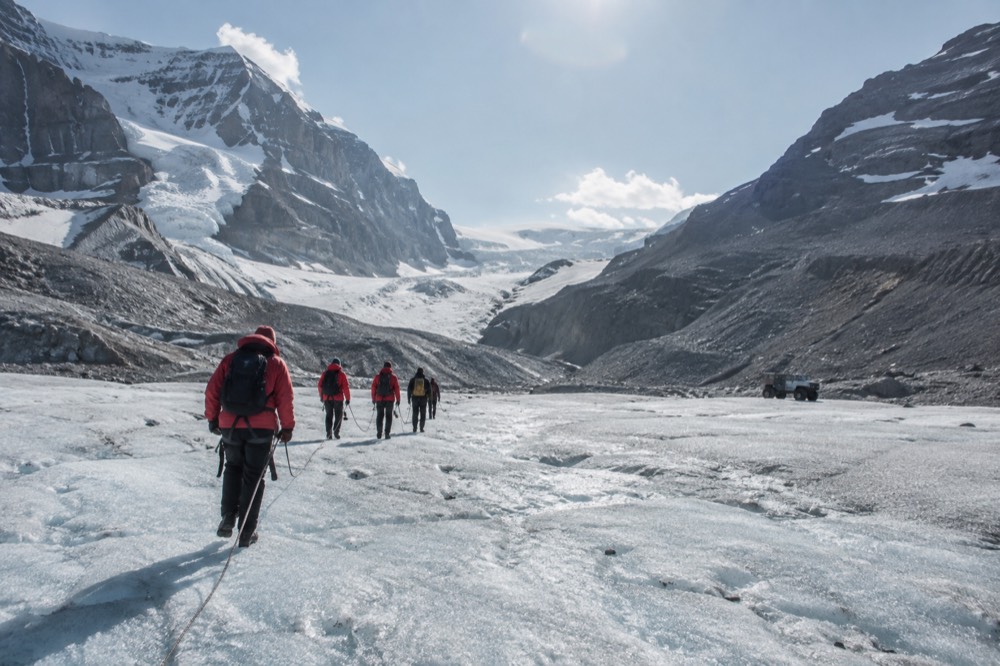A guided group in red jackets walking across a wide blue glacier ice field