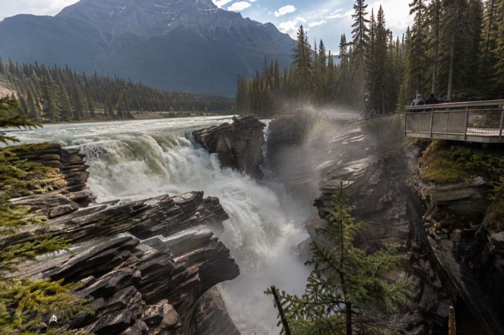 Athabasca Falls pouring through a narrow quartzite gorge, with mist rising and a viewing platform along the canyon wall.