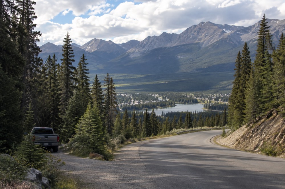 A winding road through a forested mountain valley under a wide sky
