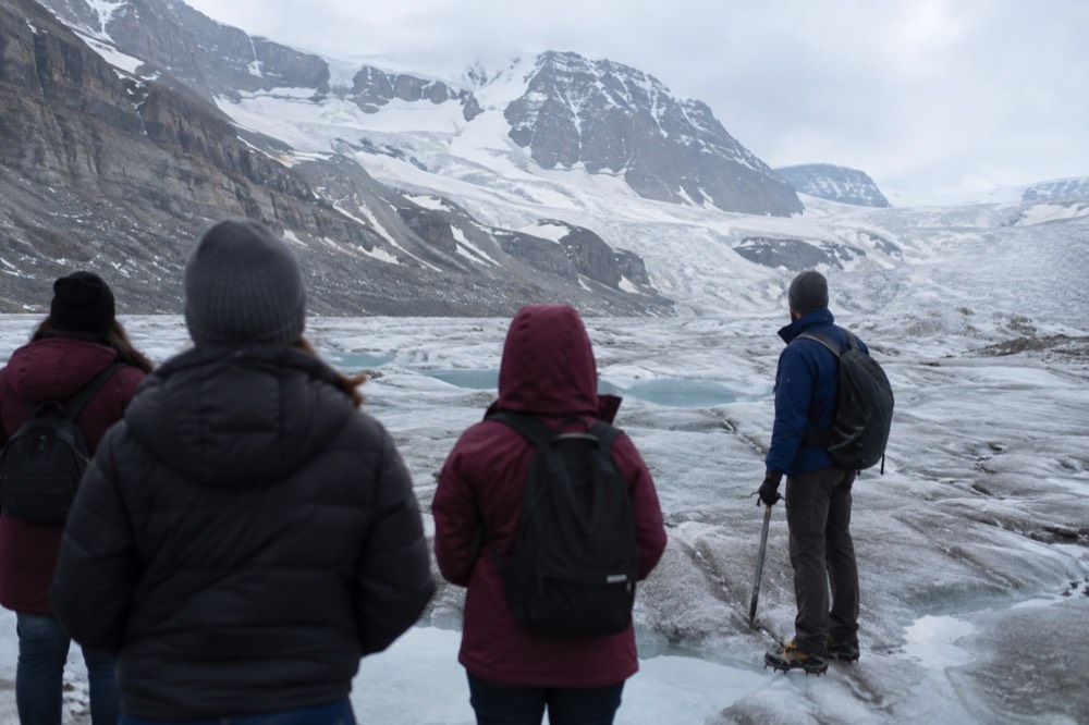 Visitors in warm jackets standing on the Athabasca Glacier beside a guide