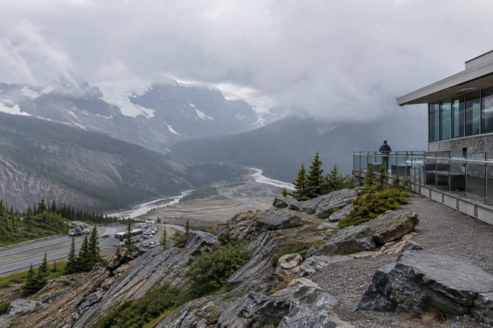 Wide view of a glacial valley from a cliff-edge platform with layered mountain ridges fading into haze