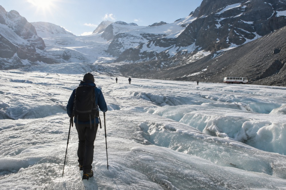 Hiker in layered clothing and warm hat standing on a glacier holding trekking poles