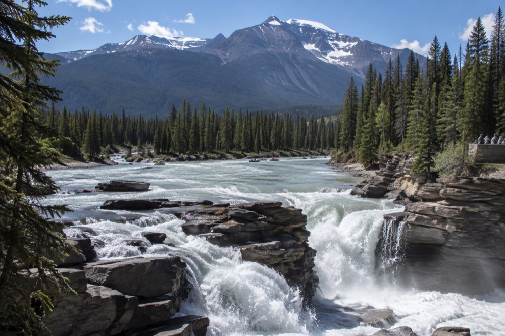 A blue glacial river cutting between forested banks under a wide sky