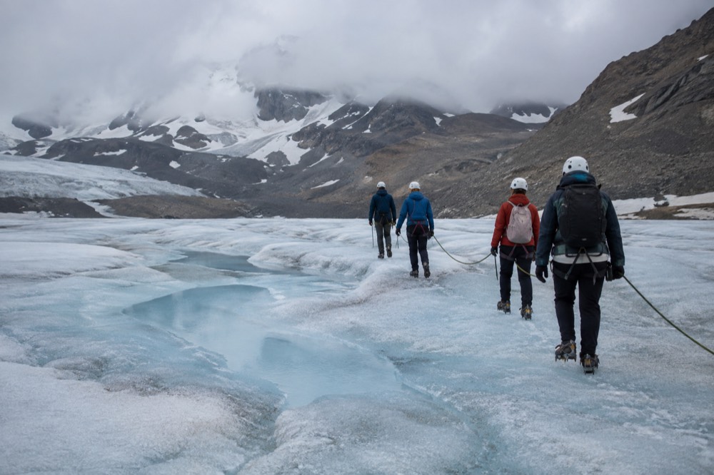 A small guided group in crampons walking across the blue ice surface of a glacier