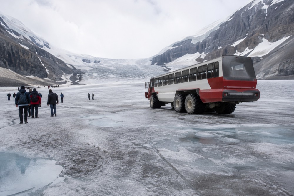 A large all-terrain vehicle with oversized wheels parked on a wide expanse of grey glacial ice