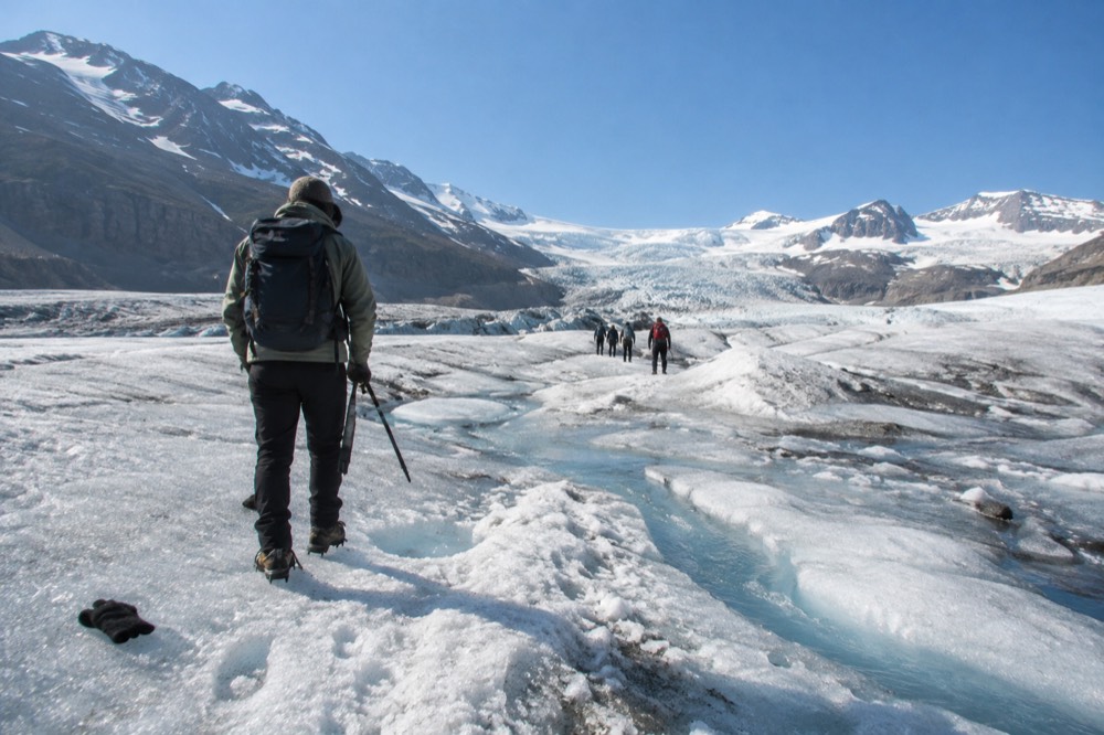 A line of hikers in crampons walking across rippled blue ice on a glacier under a clear sky