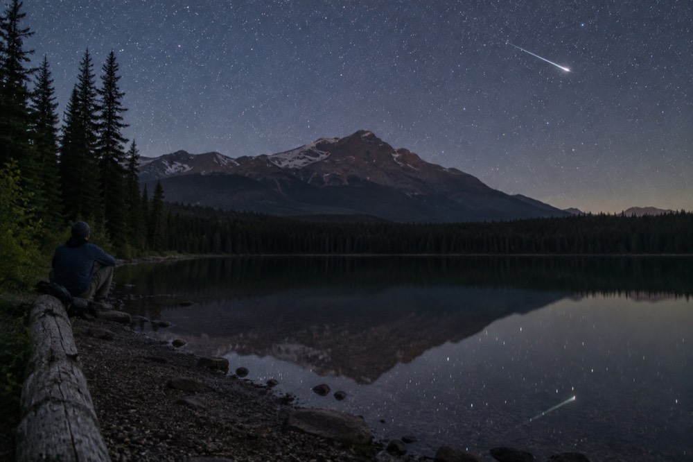 A meteor streaking over a still mountain lake at night