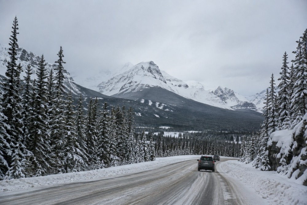 A snow-covered mountain highway curving toward distant peaks under grey skies