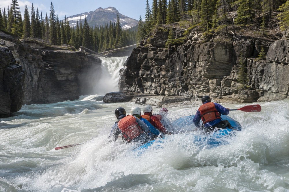 A raft plunging through a standing wave with spray over paddlers in helmets