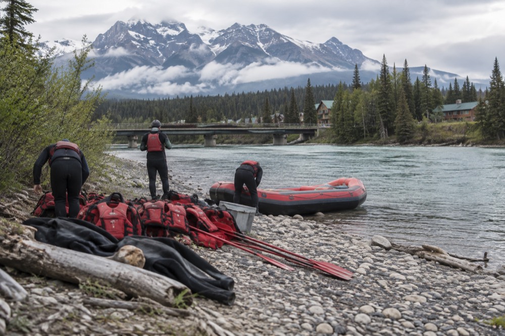 Wetsuits, life jackets and paddles laid out on a riverbank beside a raft