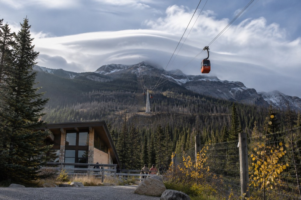 Tramway cables and cabins against dramatic clouds over a mountain summit in autumn light