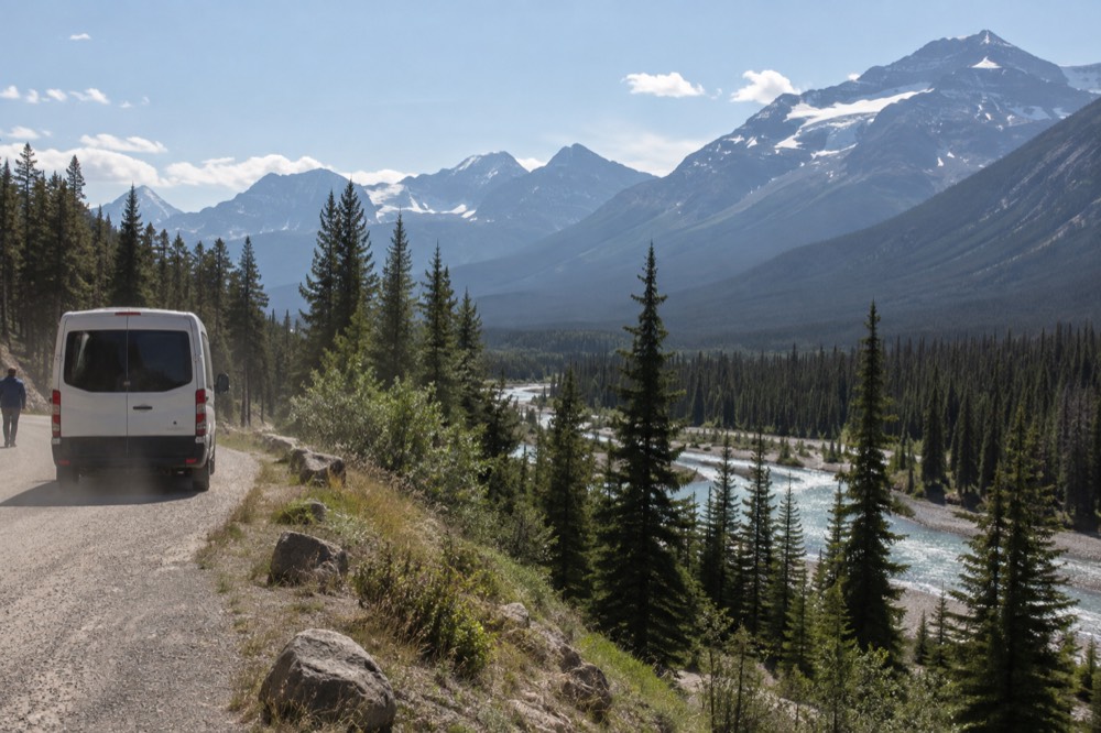 A tour van on a mountain road beside a river with forested valley walls