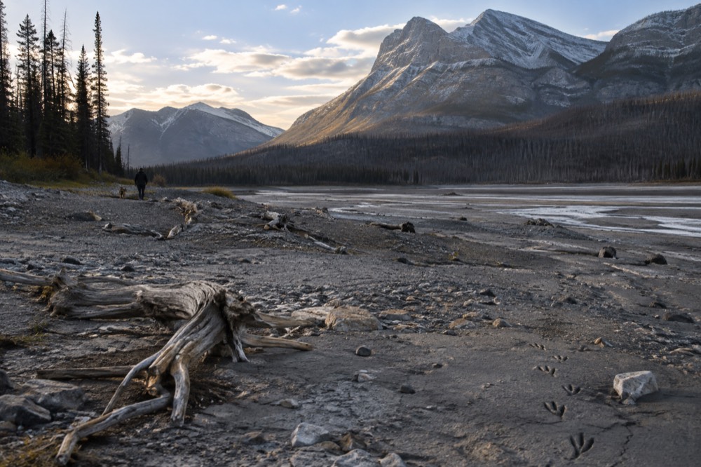 A calm lake ringed by mountains with a gravel shoreline in the foreground