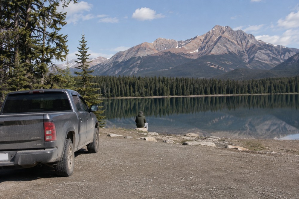 A parked vehicle at a lakeside lot with mountains reflected in still water