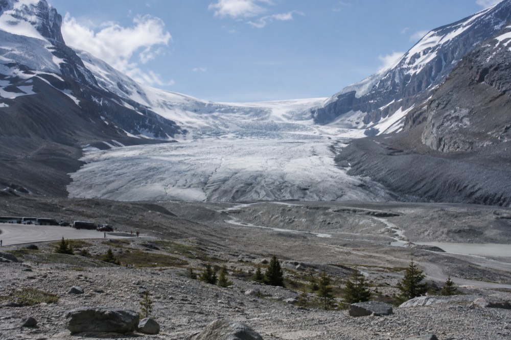 Vast icefield spilling between dark rock peaks under a pale blue sky, with a glacier tongue reaching down a valley