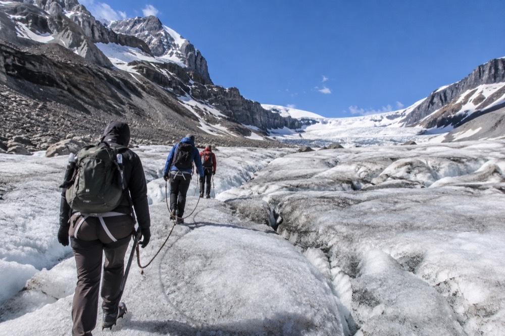A group of hikers roped together walking on a glacier under a bright blue sky