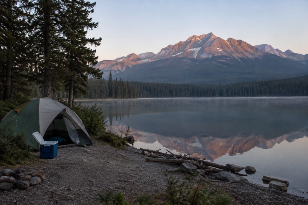 A tent pitched beside a lake with tall mountains reflected in still water